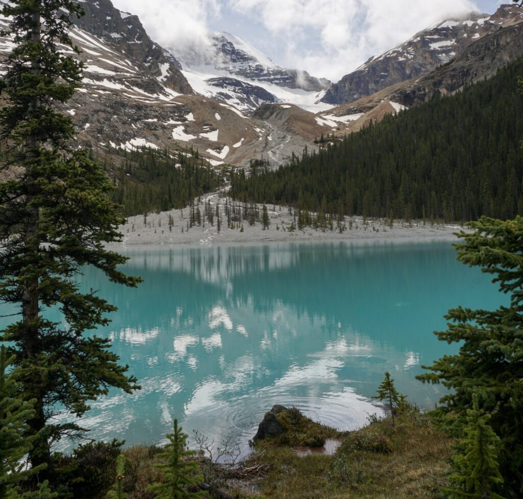 View of Boundary Lake. The water is bright blue, surrounded by mountains and pine trees.