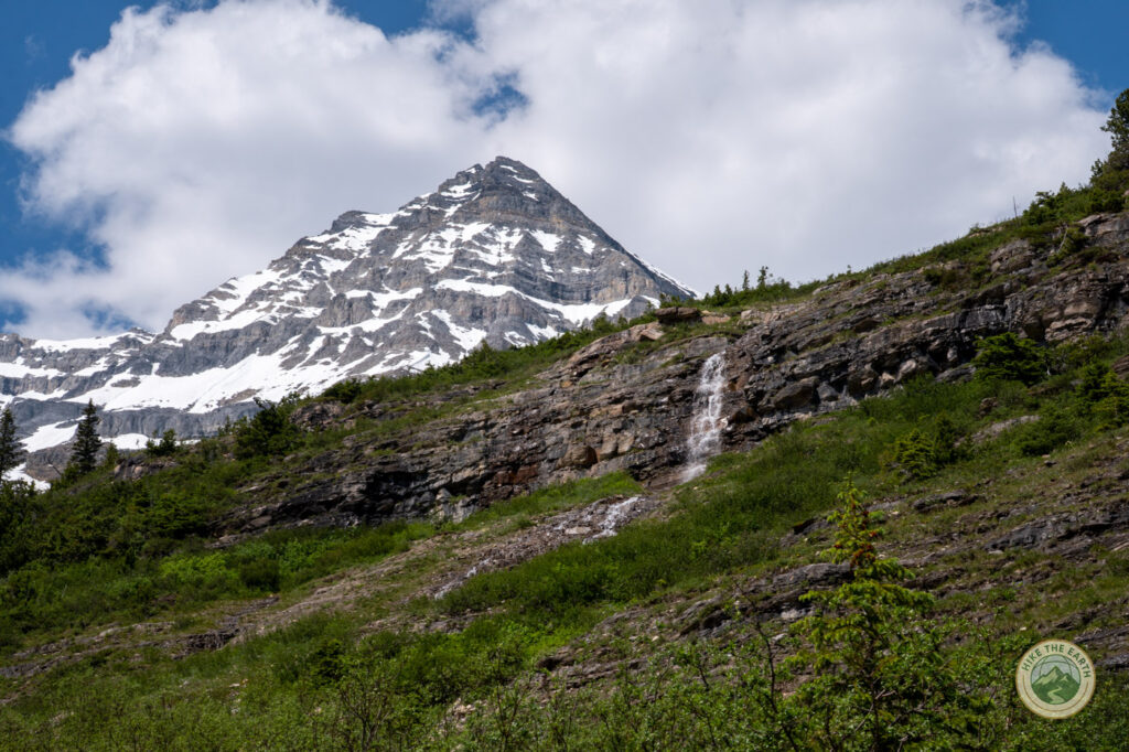  A waterfall spilling down a rock face with a snow capped peak behind it near the Plain of Six Glaciers Tea House 